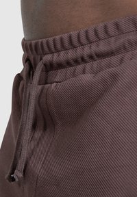 Bruine textuurshorts met een elastische tailleband en een trekkoord. Heeft ribbelaccenten en een zijzak. Close-up detail.