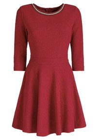Robe rouge en tissu texturé, décolleté arrondi et manches trois-quarts. Jupe évasée avec une taille cintrée, accentuée d'un col orné de bijoux.