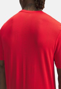 Maglietta sportiva rossa con un tessuto testurizzato e traspirante. Presenta un collo a giro e un marchio verticale sul retro. Maniche corte.