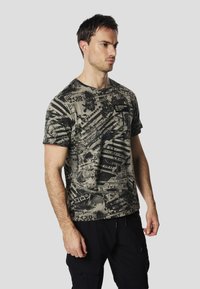 Short-sleeve t-shirt in olive green with a black graphic print featuring various text and pattern designs. Cotton blend fabric, crew neck.