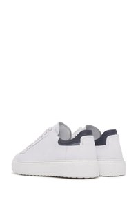 Un par de zapatillas blancas de caña baja con acentos de talón en gris oscuro y suelas de goma blancas, mostradas desde un ángulo posterior sobre fondo blanco.