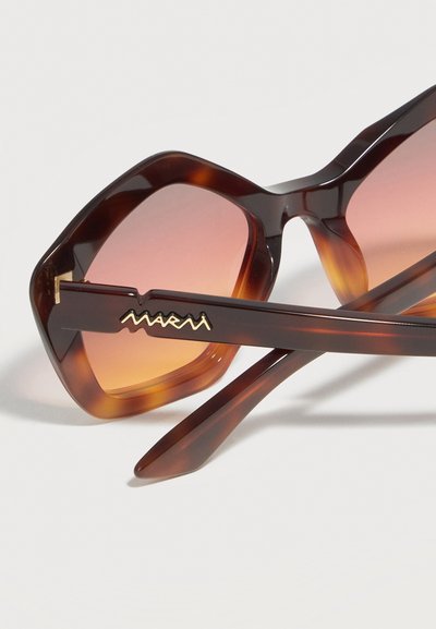 Brown tortoiseshell hexagonal sunglasses with gradient orange lenses and gold logo detail on the temple arm against a white background.
