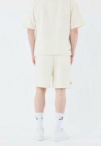 Camisa de manga corta de color crema claro y pantalones cortos a juego, hechos de un tejido texturizado, con un sutil patrón de rayas. Zapatillas blancas y calcetines incluidos.