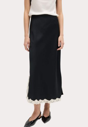 Vrouw met een zwarte midirok met witte kanten rand aan de zoom en een witte mouwloze top, gecombineerd met zwarte slingback schoenen met een puntige neus.