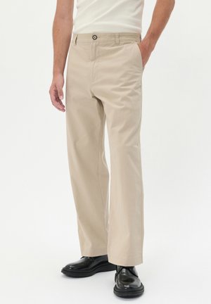 Beige cotton pants with a straight-leg design, featuring side pockets and a button closure, worn with black shoes. Smooth texture.