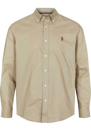 Gros plan sur une personne en train de boutonner le poignet d’une chemise beige à manches longues avec un petit détail rayé rouge, blanc et bleu.