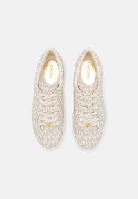 Beige sneakers with a textured fabric featuring an MK logo pattern, gold hardware accent, and white rubber sole. Lace-up design.