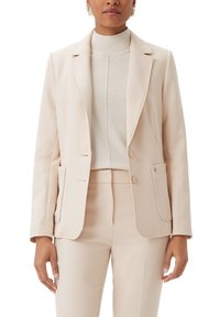 Blazer beige con collo a punte, chiusura a un bottone, due tasche frontali e superficie liscia; abbinato a un maglione leggero sottostante.