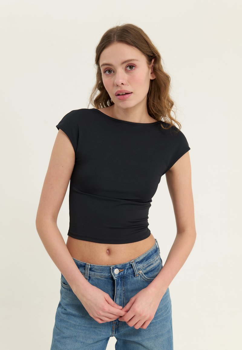 Fekete, rövid ujjú, crop top, sima textúrával és kerek nyakkivágással, világoskék, magas derekú farmernadrággal párosítva.