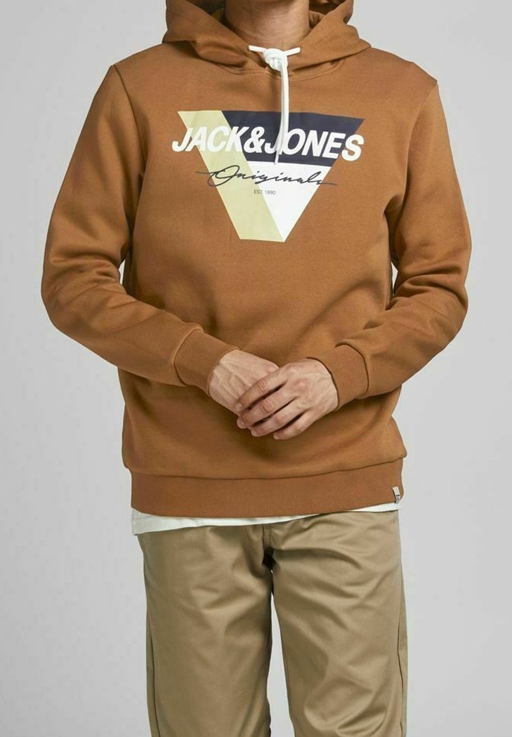 Felpa marrone con un logo triangolare blu, giallo e bianco, con cappuccio regolabile e polsini a coste. Abbinata a pantaloni beige.