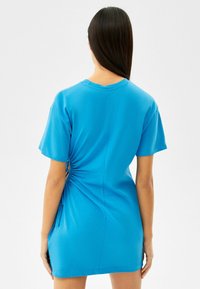 Niebieska bawełniana sukienka z krótkimi rękawami, z bocznymi marszczeniami podkreślającymi sylwetkę. Prosty okrągły dekolt i gładka faktura.