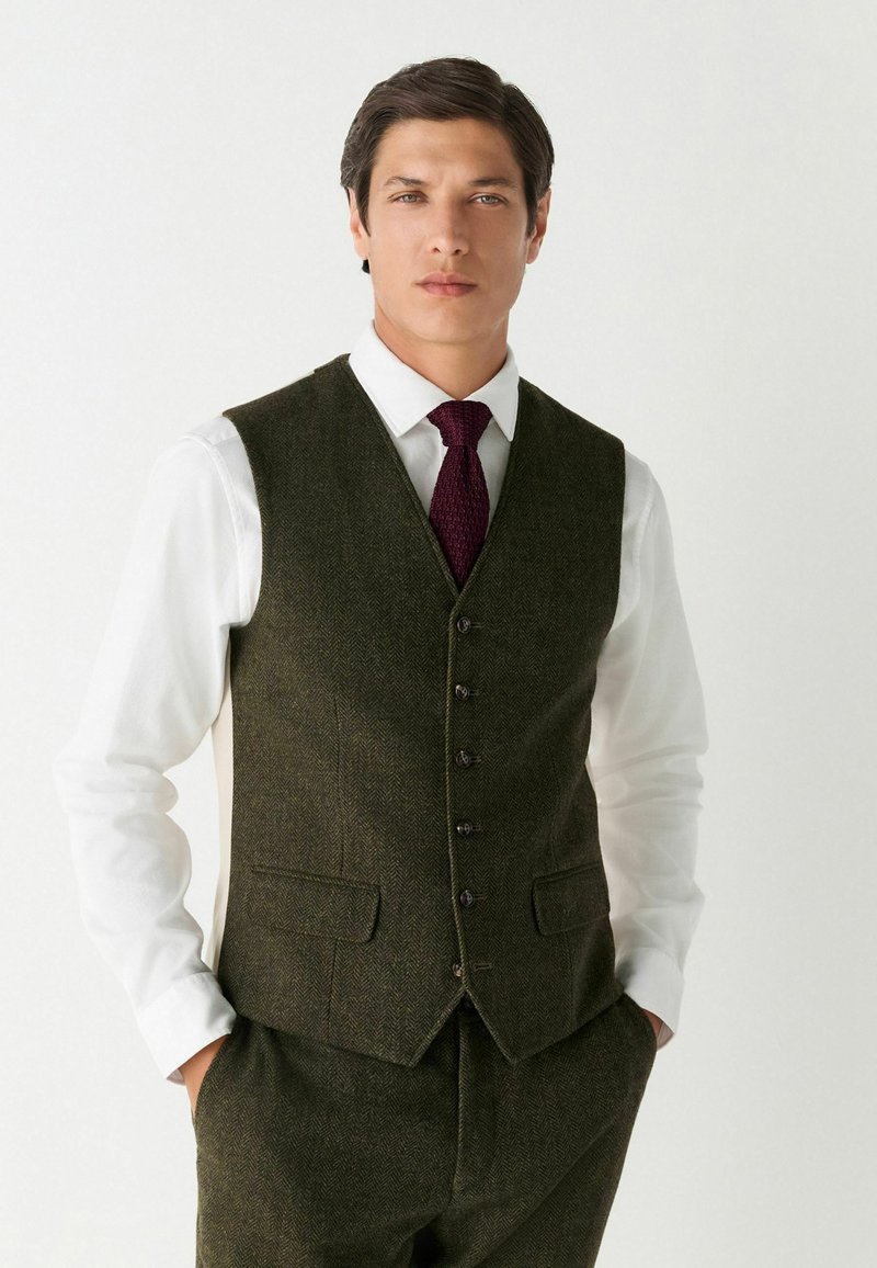 Sötétzöld halszálkás mintájú waistcoat, hat gombbal, fehér inggel és textúrált bordó nyakkendővel párosítva. Testre szabott fazon.