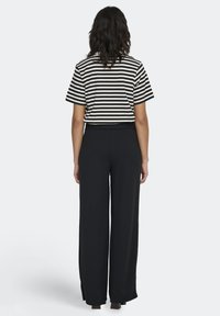 Stribet sort-hvid kortærmet top kombineret med højtaljede sorte bukser med vide ben, der har en glat tekstur og afslappet pasform.