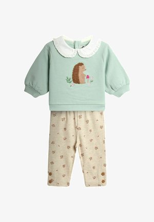 Šviesiai žalia kūdikio palaidinė ilgomis rankovėmis su baltu raukiniu apykakle ir ežio siuvinėjimu, derinama su smėlio spalvos gėlėtomis tamprėmis su sagų detalėmis.