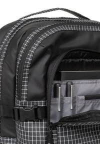 Zaino a scacchi bianco e nero con un esterno sintetico liscio, scomparto con zip e interno grigio dotato di portamatite e tasca.
