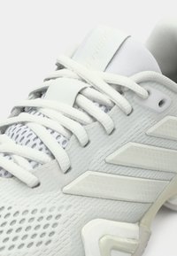 Λευκό αθλητικό παπούτσι με ανάγλυφη επάνω επιφάνεια, πάνελ από δίχτυ και τρεις διαγώνιες ρίγες. Διαθέτει επίπεδα κορδόνια και ενισχυμένη φτέρνα για υποστήριξη.