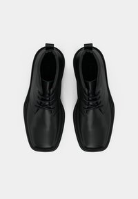 Černé kožené boty s hladkým povrchem, kulatou špičkou, šněrovacím designem a poutkem na zadní straně. Gumová podrážka s mírným vzorkem.
