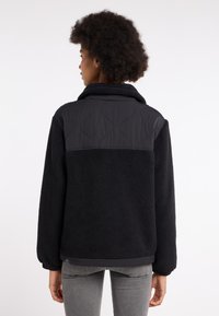 Zwarte fleece jas met een gewatteerde nylon bovenkant, voorzien van een kraag en elastische manchetten, met een gestructureerd ontwerp.
