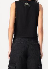 Sort cropped tank top med rund halsudskæring og ærmeløs design, med en logo detalje på ryggen. Denim cargo shorts i sort.