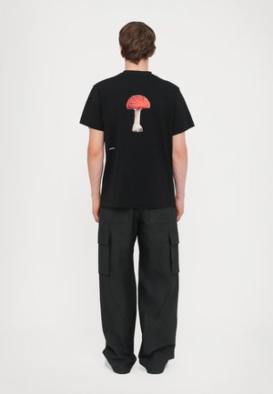Camiseta de algodón negra con un gráfico colorido de un hongo en la parte posterior. Se combina con pantalones cargo negros de corte holgado.