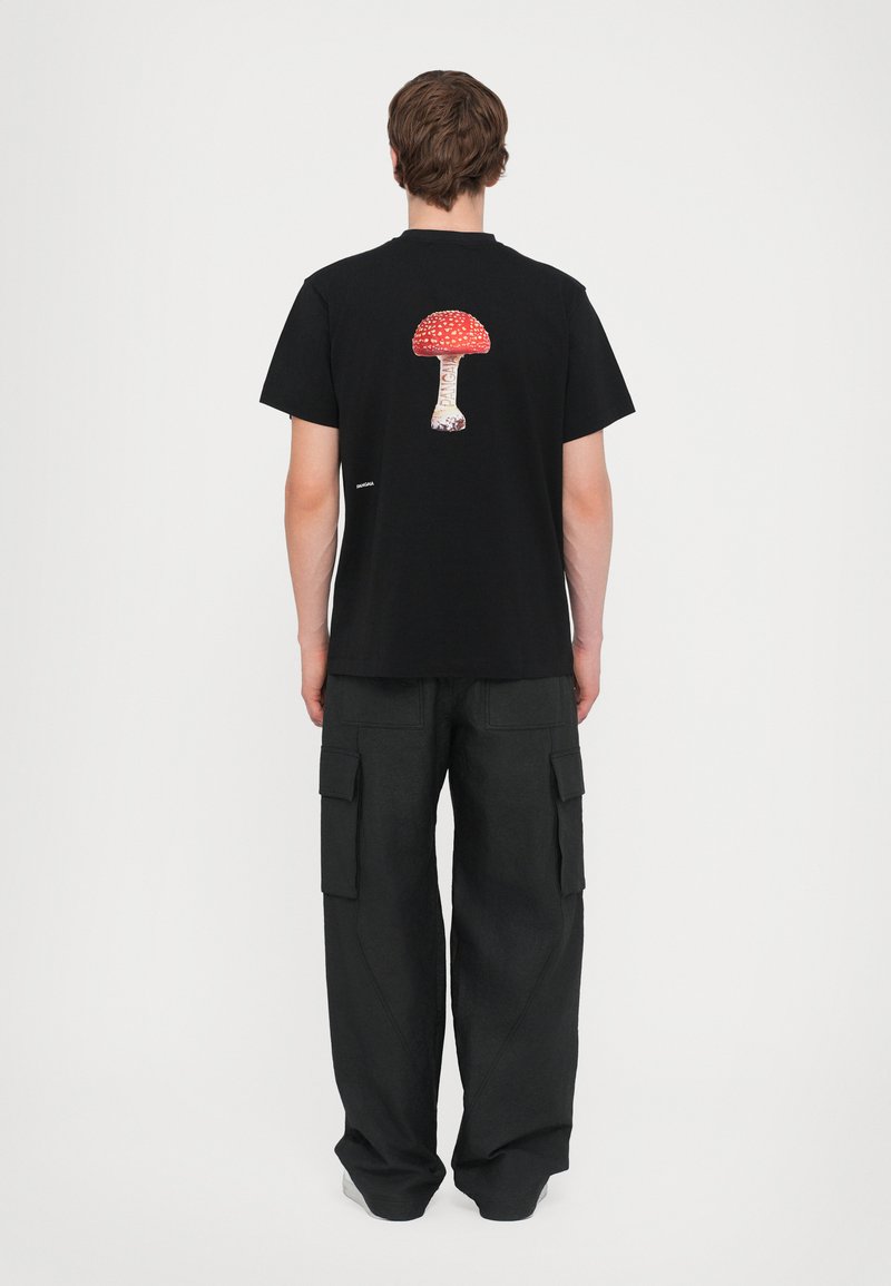 T-shirt en coton noir avec un graphique coloré de champignon au dos. Il est associé à un pantalon cargo noir ample.
