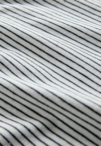 Medvilninis audinys su minkšta tekstūra, kuriame siauri juodi dryžiai ant balto fono, su švelniu blizgesiu.