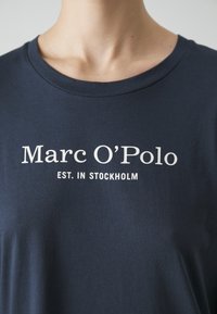 T-shirt blu navy realizzata in morbido cotone, con testo bianco: "Marc O’Polo EST. IN STOCKHOLM" in evidenza sulla parte anteriore.