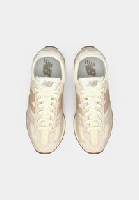 Beesed ja kreemjad New Balance'i tossud, millel on paelad, vaadatuna ülalt valgel taustal.