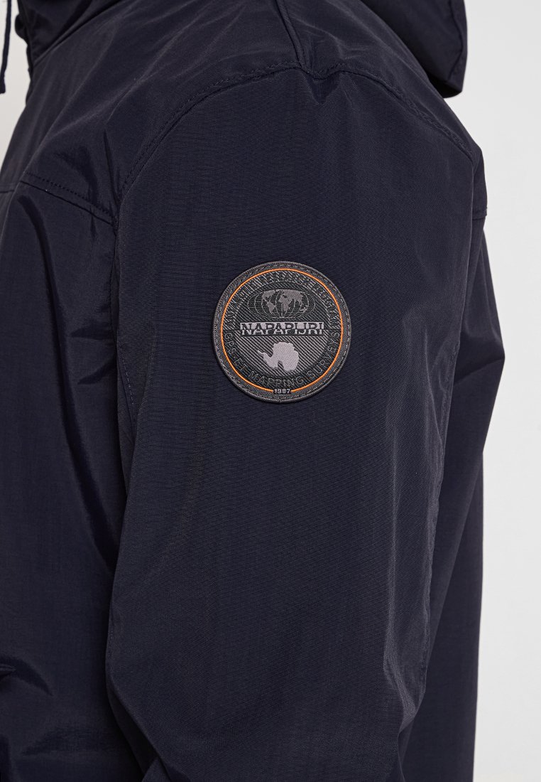 Giacca blu navy con un tessuto testurizzato. Presenta una toppa circolare sulla manica con un design di globo e elefante.