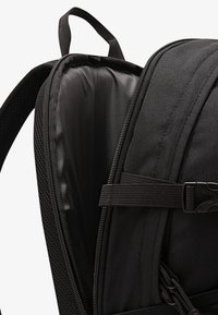 Svart ryggsekk med polstret innside, en glatt glidelås, justerbar stropp og webbing-detaljer for ekstra funksjonalitet.