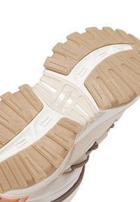 Suela de calzado con una superficie de goma beige texturizada y una entresuela blanca, diseñada para ofrecer tracción y estabilidad. Incluye ranuras y crestas.