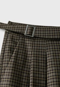 Jupe à carreaux marron et noire avec une ceinture en tissu assortie et une boucle rectangulaire argentée.