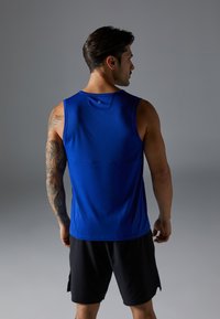 Camisola atlética azul sem mangas com um decote arredondado, textura suave e uma costura na parte de trás, combinada com calções pretos.