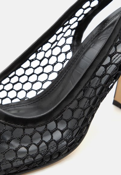 Must kõrge kontsaga king hexagonaalse võrgukujundusega, nahksete detailidega ja heledast puidust plokk-kontsaga, kujutatud lähivõttena.