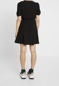 Schwarzes gestreiftes Kleid mit kurzen Puffärmeln und einem weit schwingenden Rock, getragen mit bunten klobigen Sneakers und gemusterten Socken.