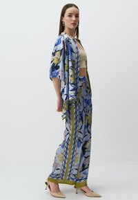 Kurtka w stylu kimono z kwiatowym wzorem oraz pasujące spodnie w odcieniach niebieskiego, żółtego i zielonego. Gładki materiał z luźnym krojem i szerokimi rękawami.