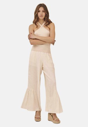 Top halter beige claro con tirantes entrelazados, combinado con pantalones fluidos de cintura alta que tienen un dobladillo acampanado y tejido texturizado.