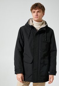 Chaqueta negra con capucha, hecha de una tela suave con un forro texturizado y suave. Cuenta con dos bolsillos frontales y un cierre de cremallera. Diseño minimalista.