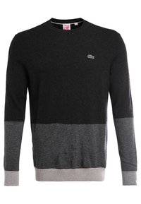 Svart och grå crewneck-tröja i stickad kvalitet med en texturerad gradientdesign och en liten grön krokodil-logotyp på bröstet.