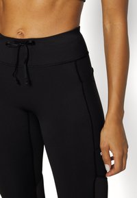 High-waisted black leggings with a drawstring waist, smooth texture, contrasting seams, and side pocket detailing.