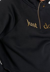 Black zip-up hoodie with gold zipper, partially visible gold text "Just do" and a small gold swoosh logo near the collar.