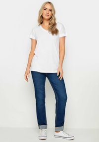 V-kauluksella varustettu valkoinen lyhythihainen T-paita, joka on yhdistetty tummansinisiin farkkuihin, joissa on käännetyt hihansuut, sekä valkoisiin sneaker-kenkiin. Yksinkertainen ja rento asukokonaisuus.