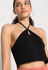 Top cropped preto tipo halter com detalhe de buraco na frente, feito de tecido suave, com alças finas e um silhueta ajustada.