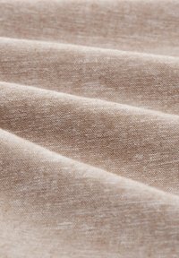 Lichtbeige stof met een textuurovervlak, met subtiele variaties in toon en een soepele val, die plooien en lagen toont.