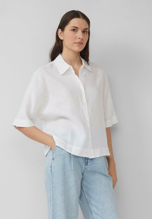 White linen short-sleeve shirt with a pointed collar and front buttons. Paired with light blue denim pants, featuring relaxed fit.