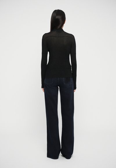 Pulover negru cu guler înalt, cu nervuri, asortat cu blugi evazați de culoare albastru închis, având un tricot texturat și mâneci lungi.
