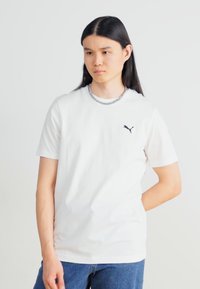 Hvit bomulls T-skjorte med en svart Puma-logo på venstre bryst, kortermet og rund hals, sammen med blå jeans.