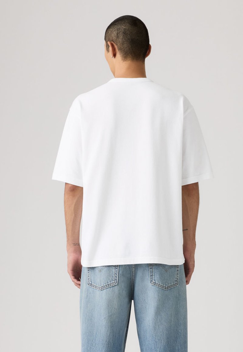 T-shirt blanc à manches courtes, tissu en coton lisse, coupe ample, encolure ronde, avec des coutures minimales et sans marque ni motif visible.