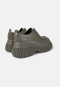 Chaussures à plateforme vertes avec une semelle striée et un design à lacets, présentant une finition brillante et un bout arrondi, vues de l'arrière.