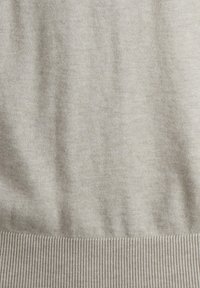 Suéter de punto en un tono beige claro con una textura suave, que presenta dobladillos acanalados y un diseño sin costuras. El material sugiere calidez y comodidad.